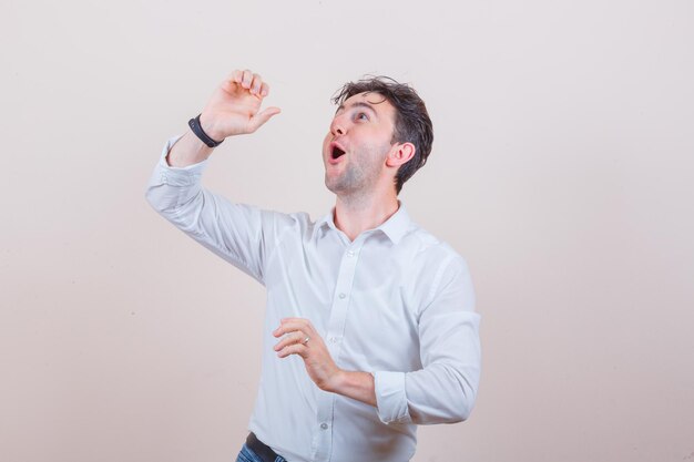 Hombre joven con camisa blanca, jeans riendo y mirando sorprendido,