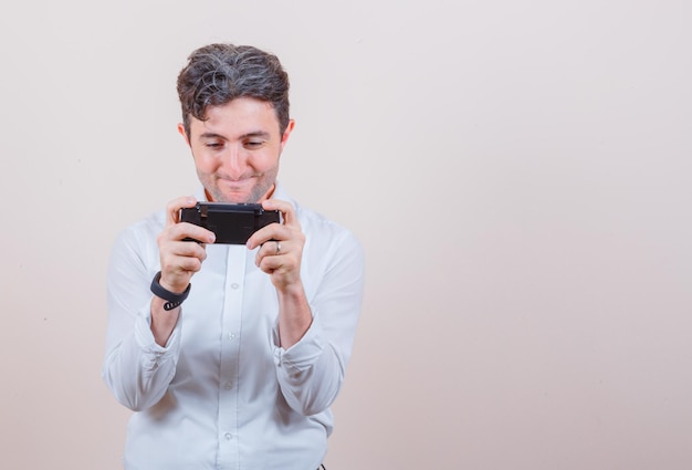 Hombre joven con camisa blanca jugando videojuegos y luciendo adicto