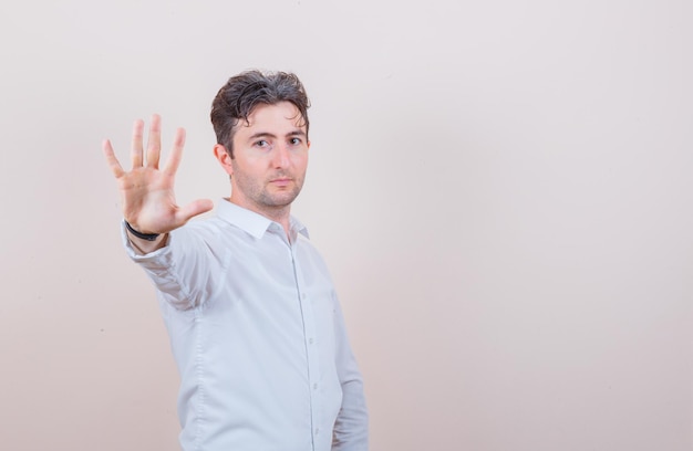 Foto gratuita hombre joven con camisa blanca mostrando gesto de parada y mirando confiado