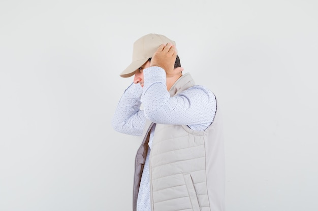 Hombre joven en camisa, chaqueta sin mangas, gorra cogidos de la mano en los oídos.