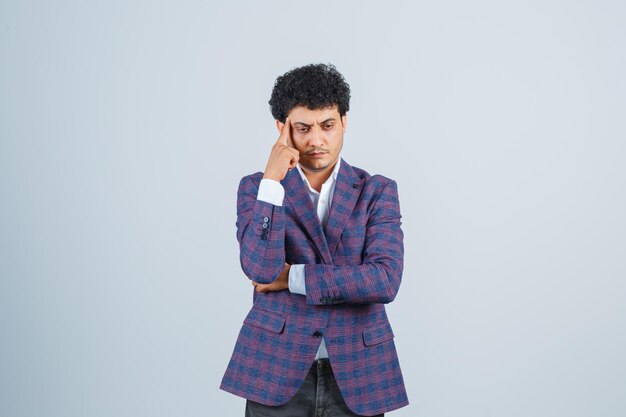 Hombre joven en camisa, chaqueta, pantalones de pie en pose de pensamiento y mirando sensible, vista frontal.