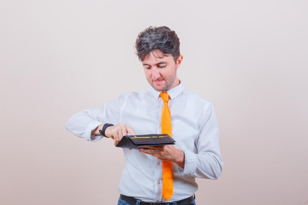 Hombre joven en camisa, corbata, jeans sacando la tarjeta de la billetera