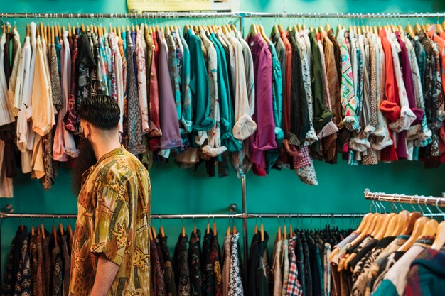 Hombre joven en camisa elegir ropa en centro comercial o tienda de ropa