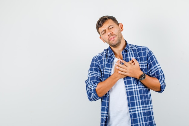 Hombre joven en camisa haciendo gesto de agradecimiento con las manos en el pecho y mirando agradecido, vista frontal.