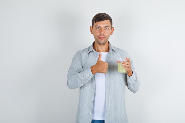 Hombre joven en camisa, jeans con vaso de jugo con el pulgar hacia arriba