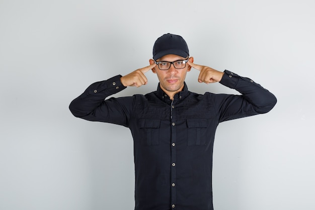 Foto gratuita hombre joven en camisa negra con gorra, gafas sosteniendo los dedos en las sienes