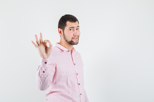 Hombre joven en camisa rosa mostrando signo ok y mirando alegre