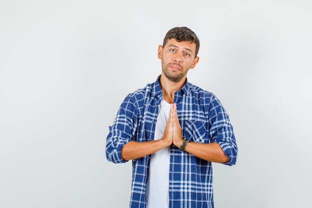 Hombre joven en camisa tomados de la mano en gesto de oración y mirando triste, vista frontal.