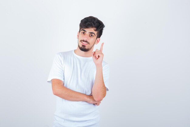 Hombre joven en camiseta apuntando hacia arriba y mirando alegre