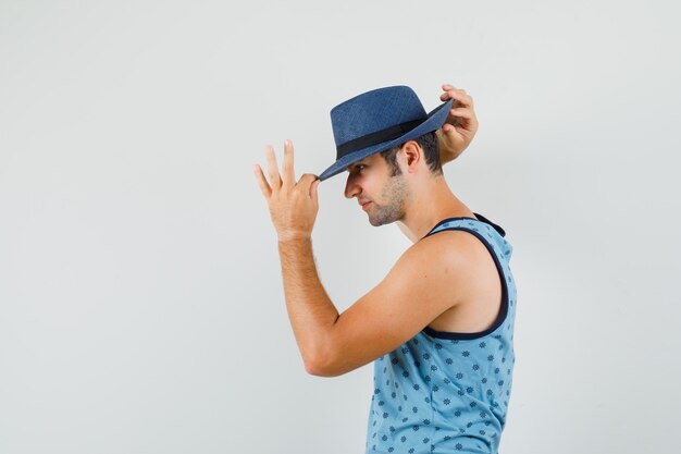 Hombre joven en camiseta azul ajustando el sombrero y luciendo guapo.