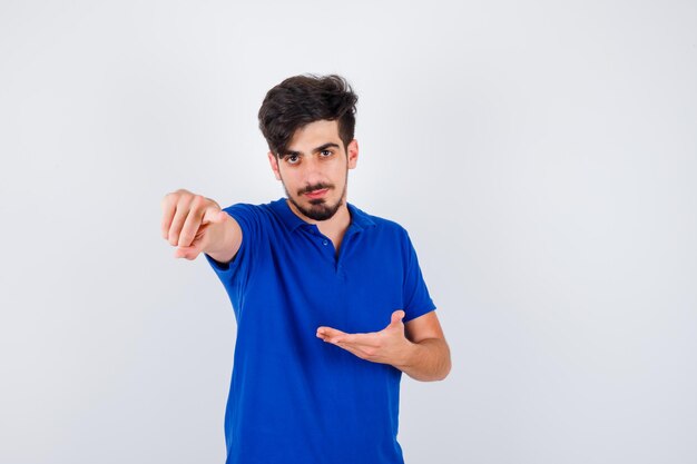 Hombre joven en camiseta azul estirando una mano mientras sostiene algo y apuntando al frente y mirando serio