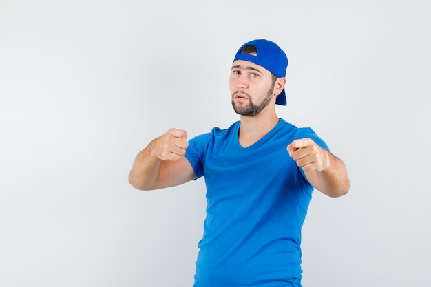 Hombre joven en camiseta azul y gorra apuntando a la cámara y mirando confiado