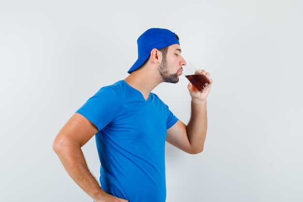 Hombre joven en camiseta azul y gorra bebiendo bebidas frías y mirando sediento