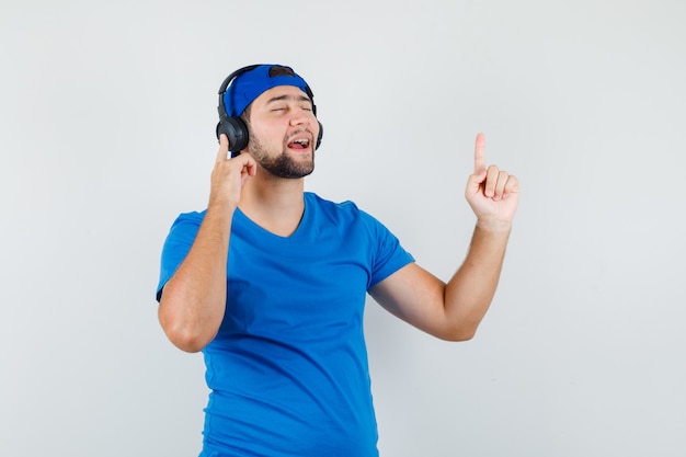 Hombre joven en camiseta azul y gorra disfrutando de la música con auriculares con el dedo hacia arriba