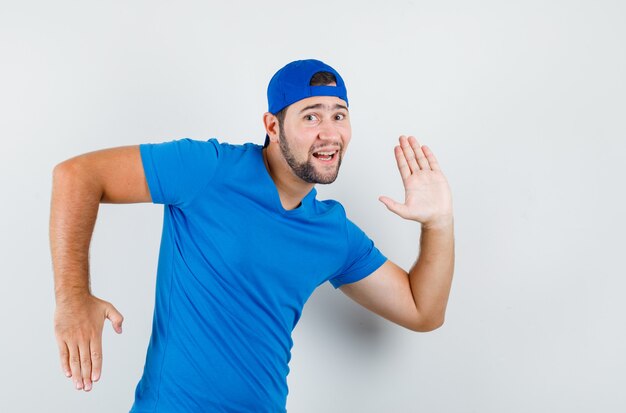 Hombre joven en camiseta azul y gorra gesticulando como hacer movimiento y mirando divertido