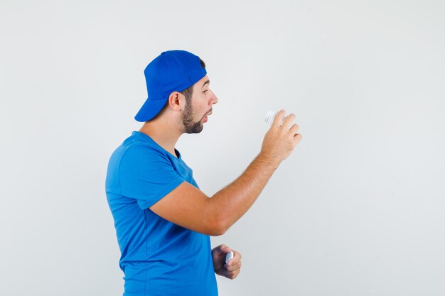 Hombre joven en camiseta azul y gorra mirando en una botella de píldoras y con curiosidad.