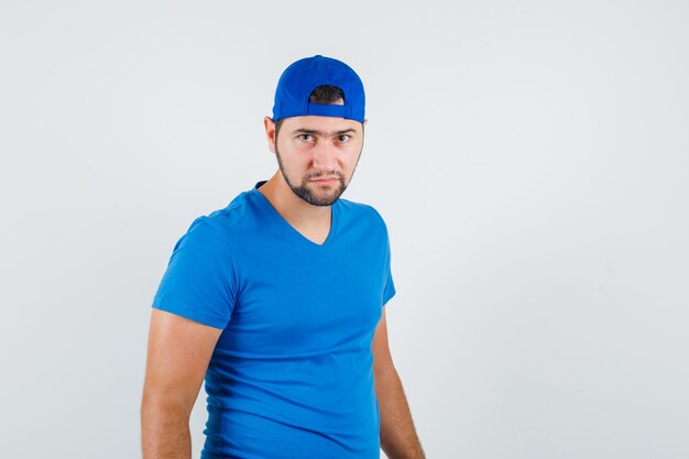 Hombre joven en camiseta azul y gorra mirando a la cámara con cuidado y mirando confiado