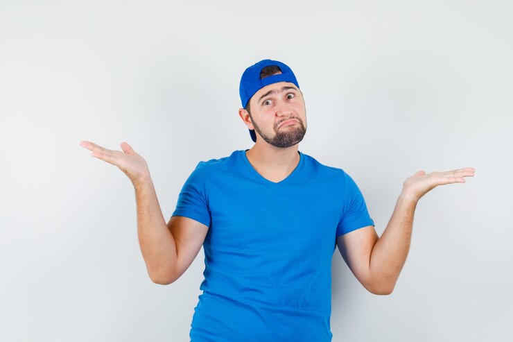 Foto gratuito hombre joven en camiseta azul y gorra mostrando gesto de impotencia y mirando confundido