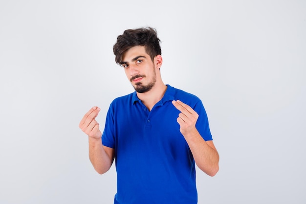 Hombre joven en camiseta azul mostrando gesto de dinero y mirando serio