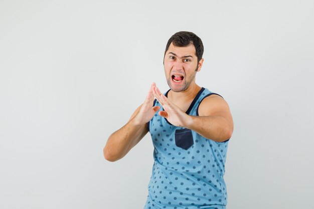Hombre joven en camiseta azul que muestra el gesto de chuleta de karate y parece poderoso