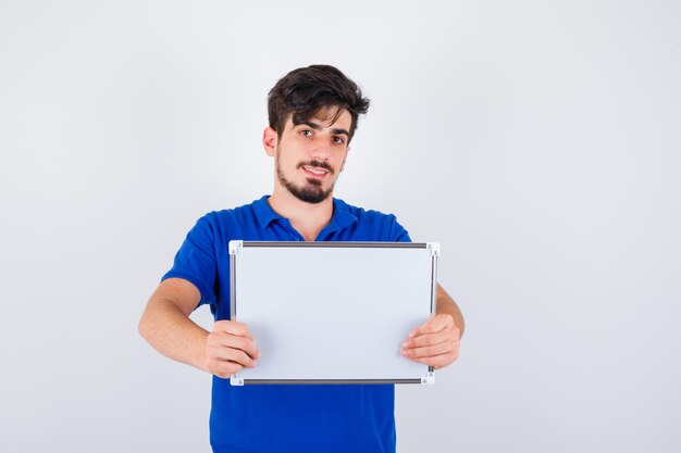 Hombre joven en camiseta azul sosteniendo pizarra y mirando feliz