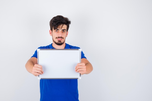 Hombre joven en camiseta azul sosteniendo pizarra y mirando feliz