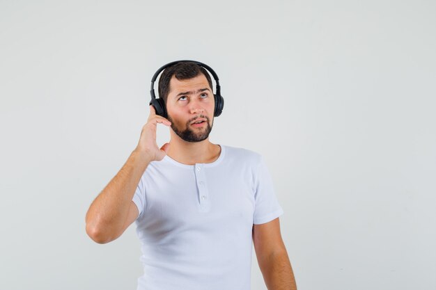 Hombre joven en camiseta blanca escuchando música y mirando concentrado, vista frontal.