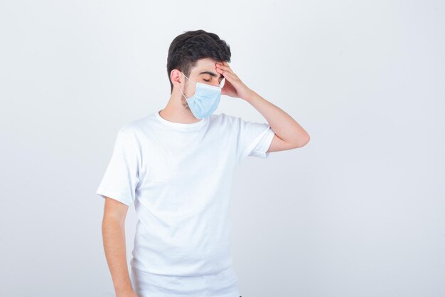 Hombre joven en camiseta blanca, máscara que sufre de tos y parece cansado