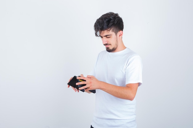 Hombre joven en camiseta blanca mirando a la billetera y mirando pensativo