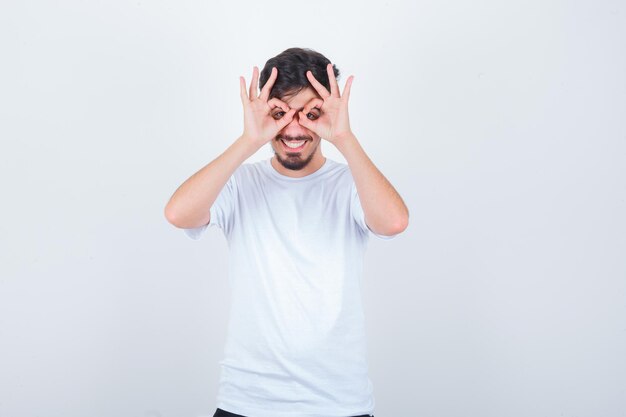 Hombre joven en camiseta blanca mostrando gesto de gafas y mirando confiado