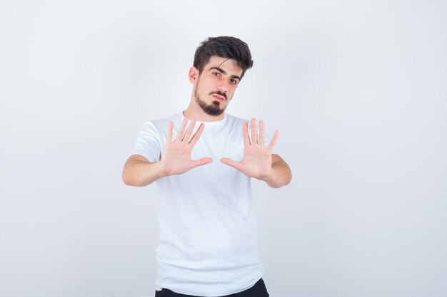 Hombre joven en camiseta blanca mostrando gesto de parada y mirando confiado