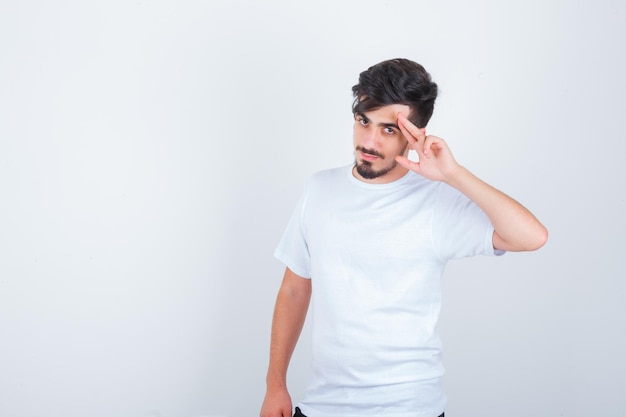 Hombre joven en camiseta blanca mostrando gesto de saludo y mirando confiado