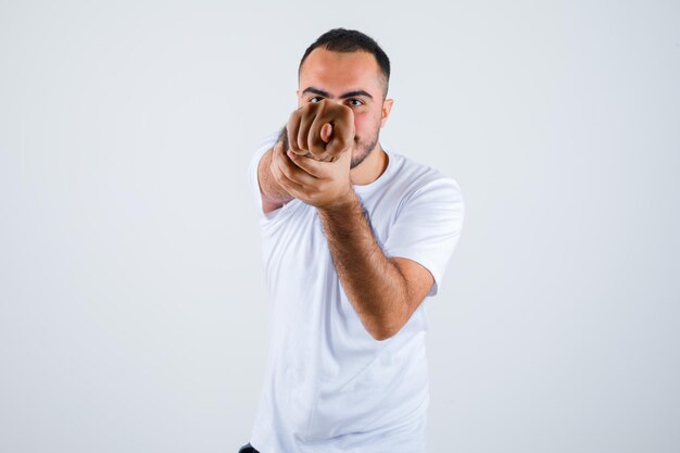 Hombre joven en camiseta blanca mostrando signo de higo y mirando grosero