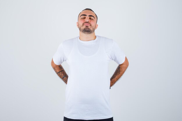 Hombre joven con camiseta blanca y pantalón negro cogidos de la mano en la cintura y mirando serio