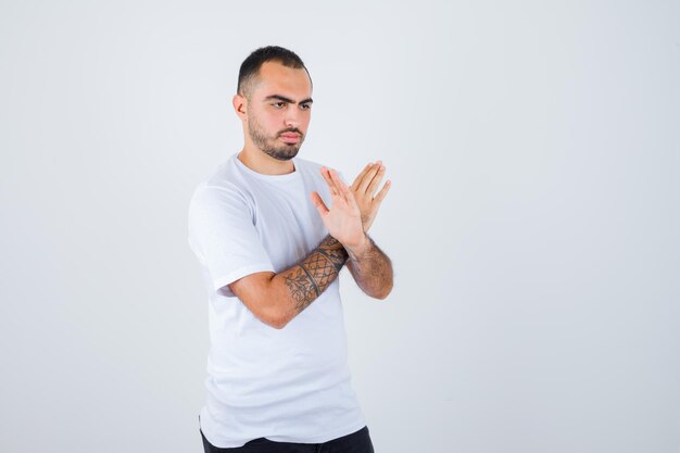 Hombre joven en camiseta blanca y pantalón negro mostrando gesto x y mirando serio