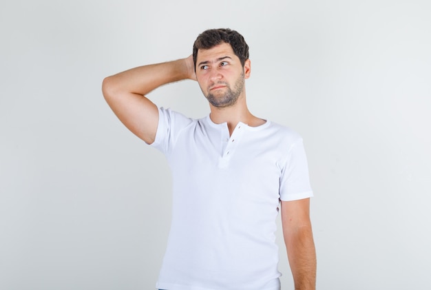 Hombre joven en camiseta blanca pensando con la mano detrás de la cabeza