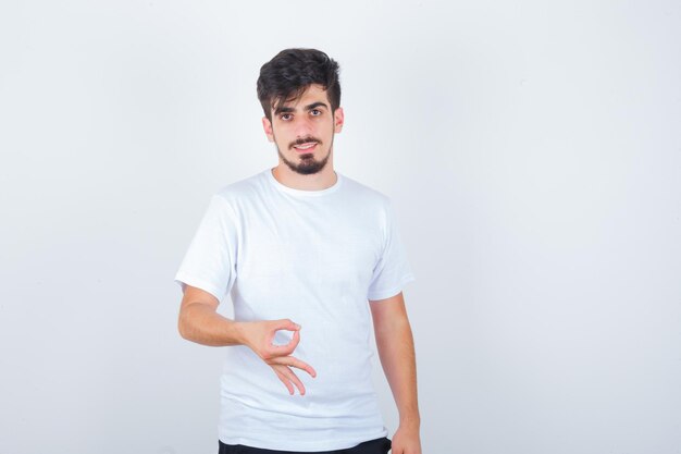 Hombre joven en camiseta blanca que muestra un gesto bien y parece confiado