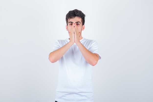 Hombre joven en camiseta blanca tomados de la mano en gesto de oración y mirando esperanzado