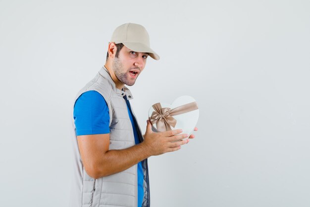 Hombre joven en camiseta, chaqueta con caja de regalo y mirando confiado.