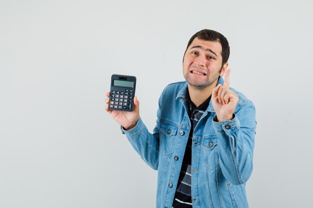 Hombre joven en camiseta, chaqueta gesticulando espera un minuto, sosteniendo la calculadora y mirando indefenso