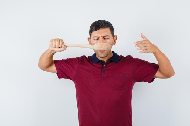Hombre joven en camiseta degustación de comida con cuchara de madera, vista frontal.
