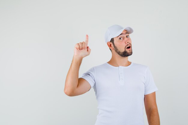 Hombre joven en camiseta, gorra apuntando hacia arriba y mirando concentrado, vista frontal.