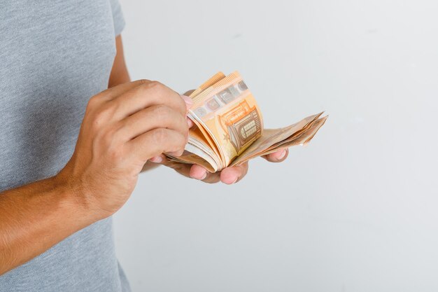 Hombre joven en camiseta gris contando billetes en euros