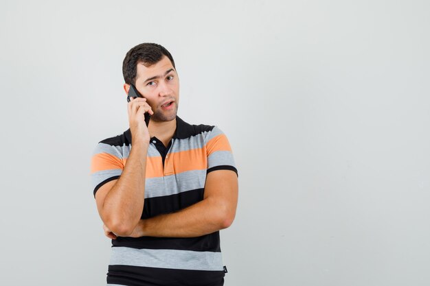 Hombre joven en camiseta hablando por teléfono y mirando pensativo