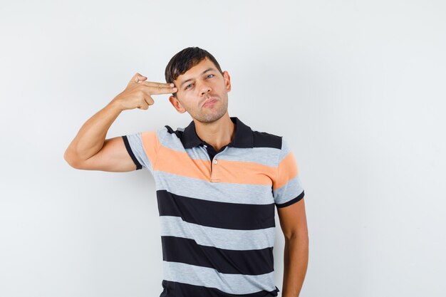 Hombre joven en camiseta haciendo gesto de suicidio y mirando serio