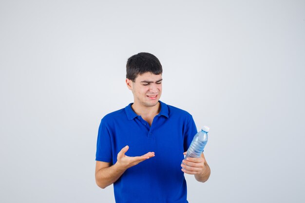 Hombre joven en camiseta mostrando una botella de plástico y mirando disgustado, vista frontal.