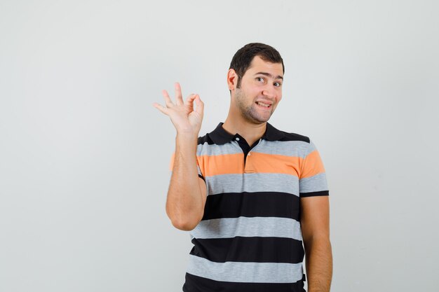 Hombre joven en camiseta mostrando gesto ok y mirando satisfecho