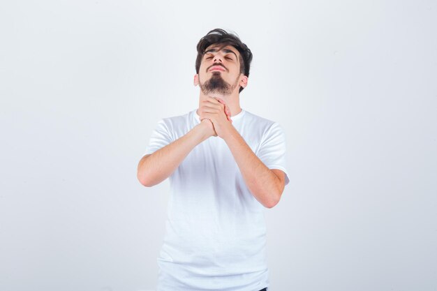 Hombre joven en camiseta mostrando gesto de oración y mirando pacífico