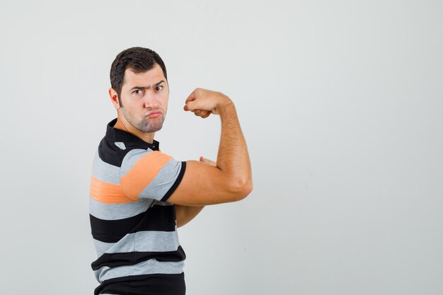 Foto gratuita hombre joven en camiseta mostrando los músculos de su brazo y buscando un espacio impresionante para texto