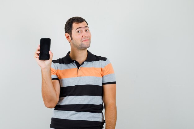 Hombre joven en camiseta mostrando su teléfono y mirando satisfecho